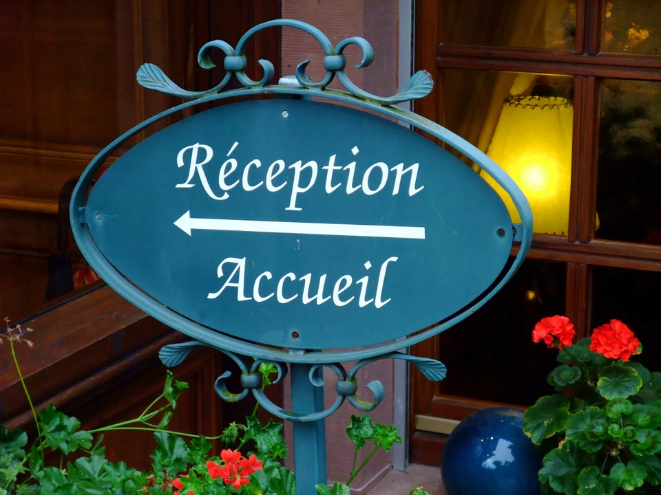 Entrée d'hôtel ou établissement d'accueil avec enseigne directionnelle bilingue français "Réception/Accueil"
