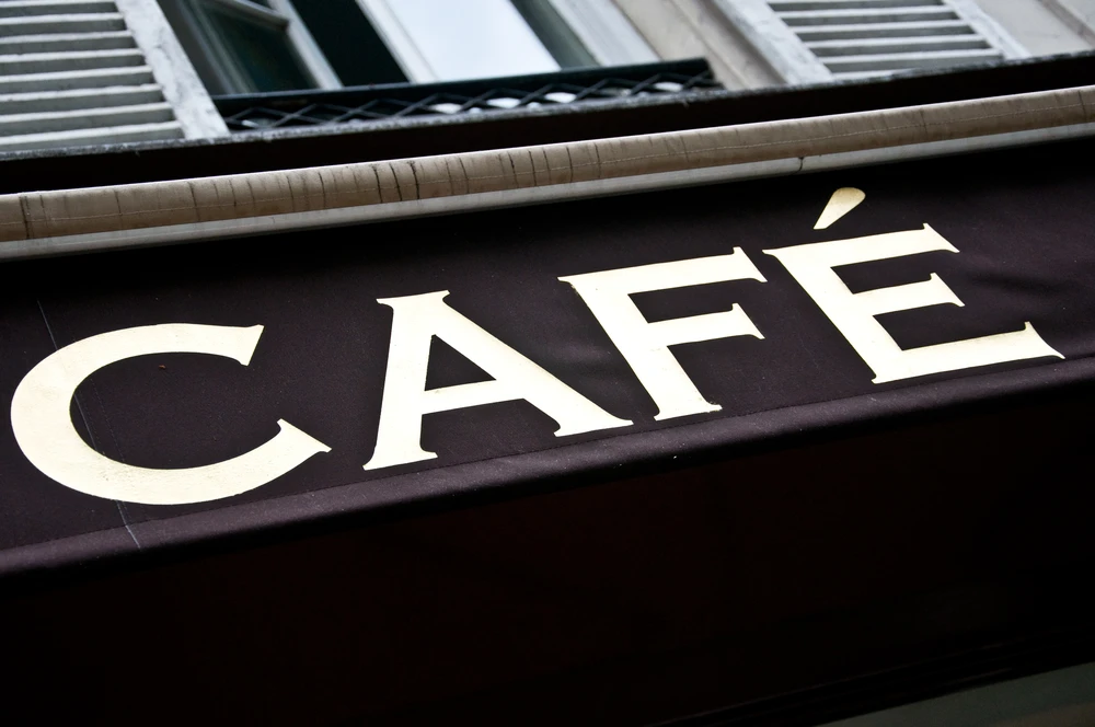 Façade extérieure d'un établissement commercial avec enseigne "CAFÉ" en lettres capitales blanches sur fond noir mat