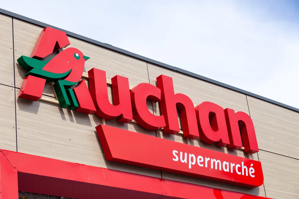 Façade extérieure d'un supermarché Auchan avec enseigne rouge en lettres volumineuses 3D et logo oiseau stylisé vert
