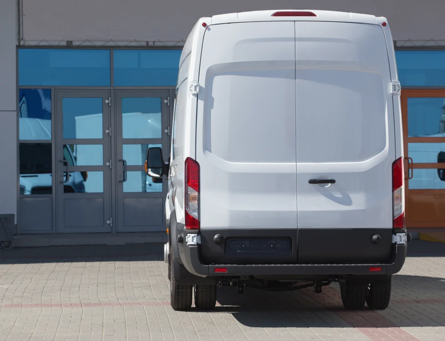 Véhicule utilitaire blanc stationné devant un bâtiment commercial avec façade vitrée et portes coulissantes