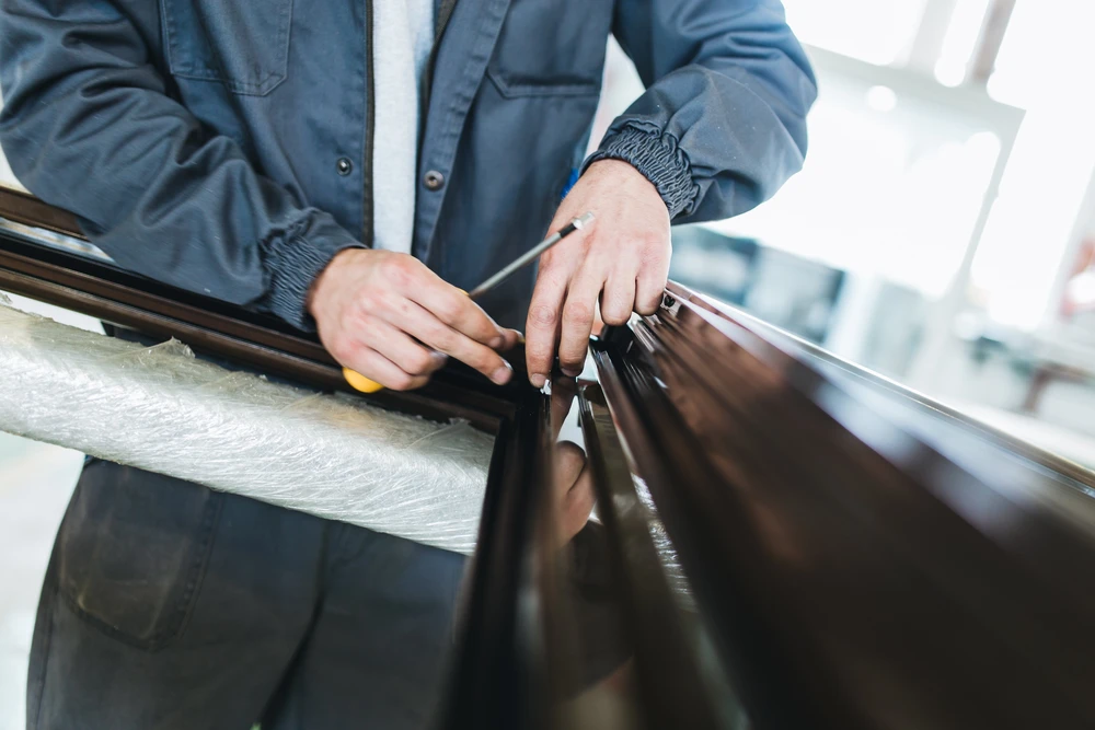 Un professionnel en combinaison bleue applique un film teinté sur la vitre d'un véhicule noir dans un atelier automobile