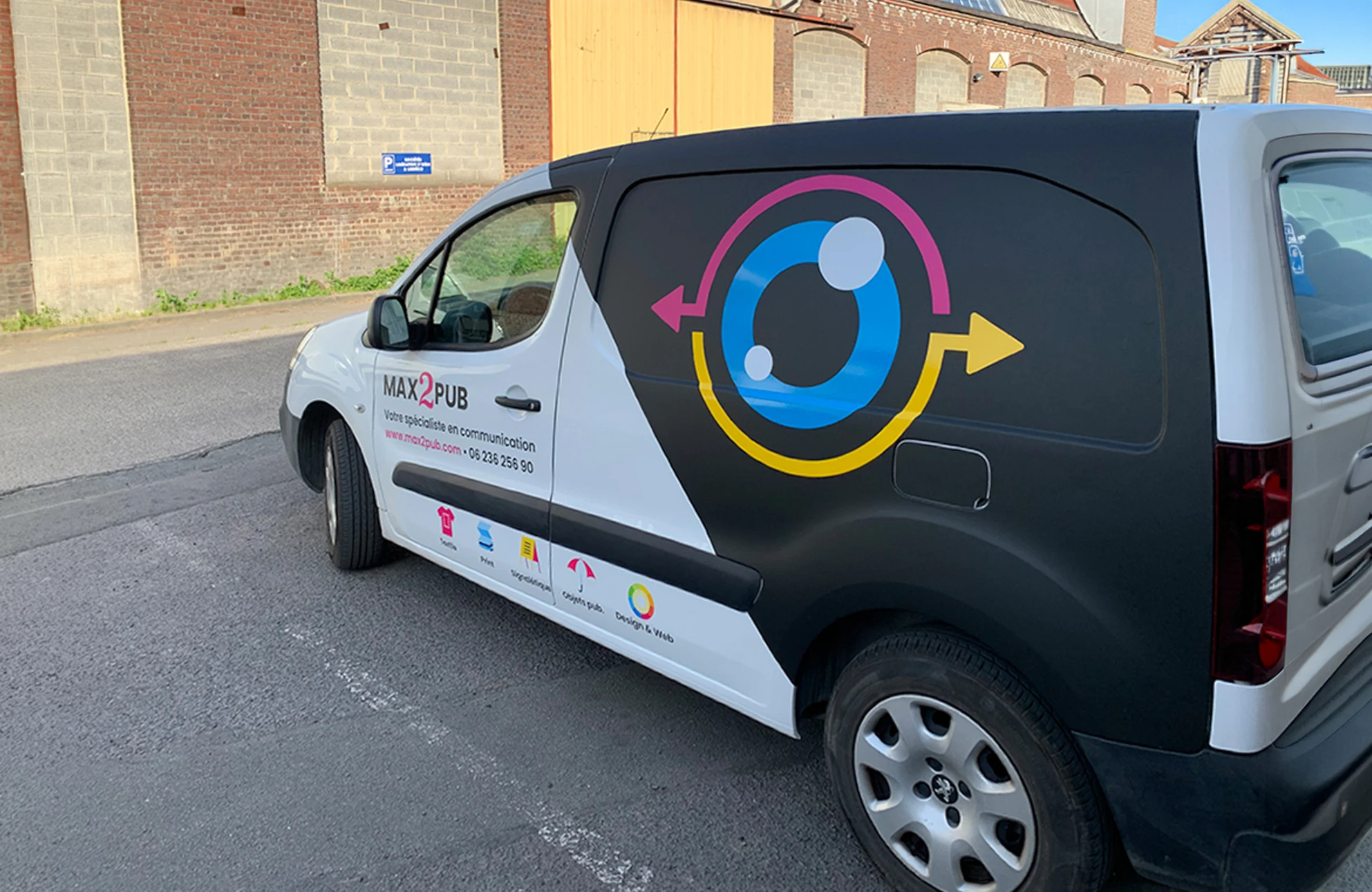 Photographie d'un véhicule berline ou monospace de couleur foncée circulant ou stationné en milieu urbain, recouvert d'un covering complet aux couleurs vives et design professionnel, présentant clairement la transformation visuelle du véhicule par le covering. L'image doit montrer le véhicule en situation réelle (rue, quartier commercial ou parking) pour illustrer son utilisation comme vitrine mobile, avec un éclairage naturel professionnel.